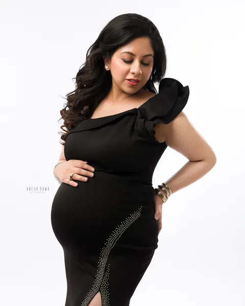 Maternity photoshoot in Delhi: expecting mother in a black one-shoulder gown with a ruffled sleeve and a crystal-trimmed side slit, hand on