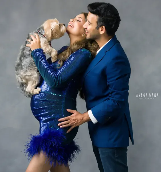Playful couple with a small dog: wife in a royal blue sequin mini dress with feather hem, husband in a navy blazer and jeans, dog licking