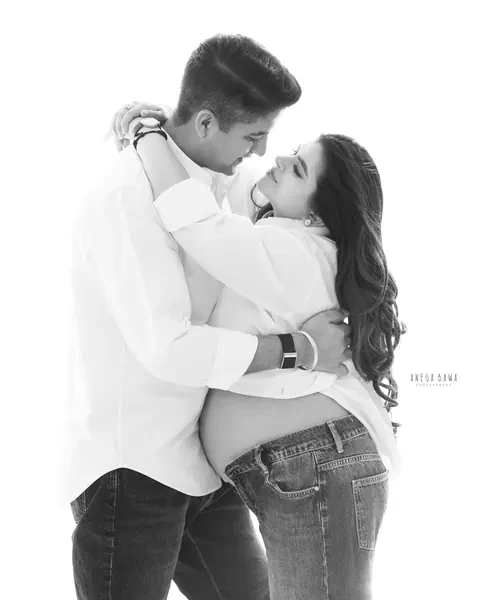 Maternity photoshoot in Delhi: black and white portrait of a couple in white shirts and jeans embracing and looking at each other, bare