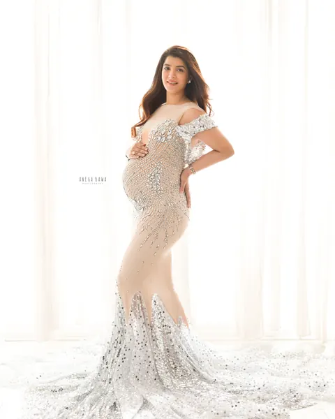 Maternity photoshoot in Delhi: smiling expecting mother in a nude mesh gown covered in crystals with a sequinned flared train, sheer