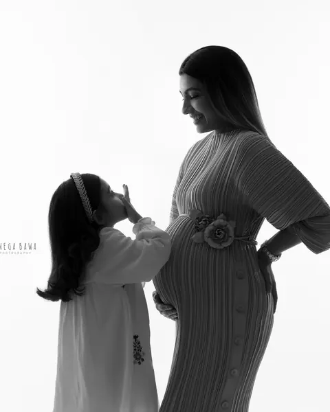 Maternity photoshoot in Delhi: black and white silhouette of a young daughter in a headband reaching up toward her expecting mother, who