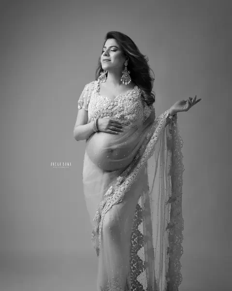 Maternity photoshoot in Delhi: black and white portrait of expecting mother in a pearl-embellished sheer net saree with statement earrings
