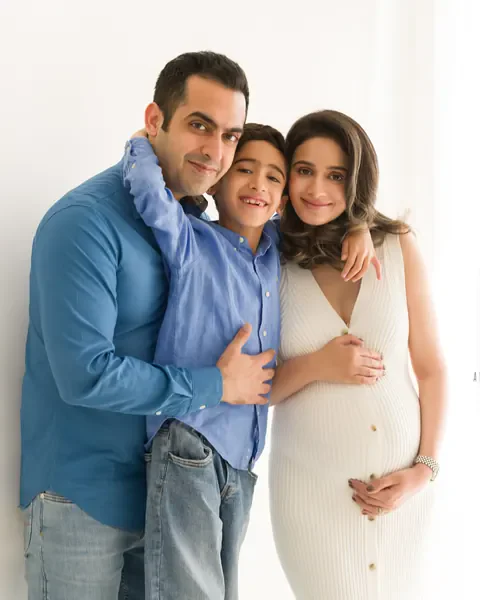 Maternity photoshoot in Delhi: smiling family of three, expecting mother in a white ribbed knit dress with her son and husband in blue