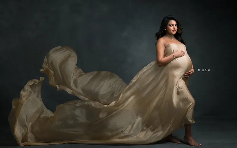 Maternity photoshoot in Delhi: expecting mother in a strapless gold silk drape with the fabric flowing out behind her, walking barefoot