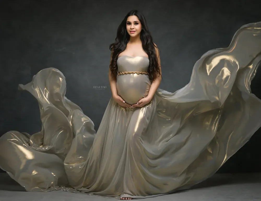 Expecting mother in a pearl-gold metallic strapless gown with a gold chain belt and a vast sheer metallic train flying out on both sides