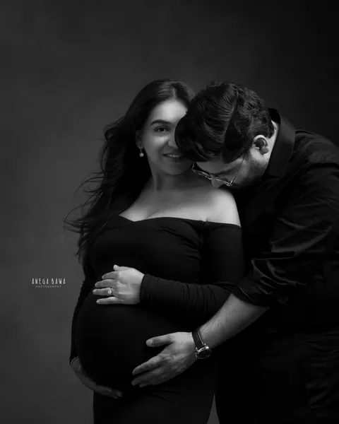 Maternity photoshoot in Delhi: black and white portrait of a husband in glasses nuzzling his smiling wife's shoulder, she wears an