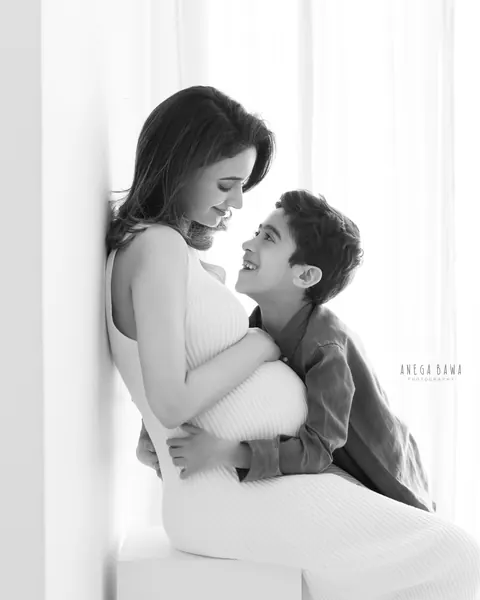 Maternity photoshoot in Delhi: black and white portrait of a son looking up at his expecting mother, she wears a sleeveless ribbed knit