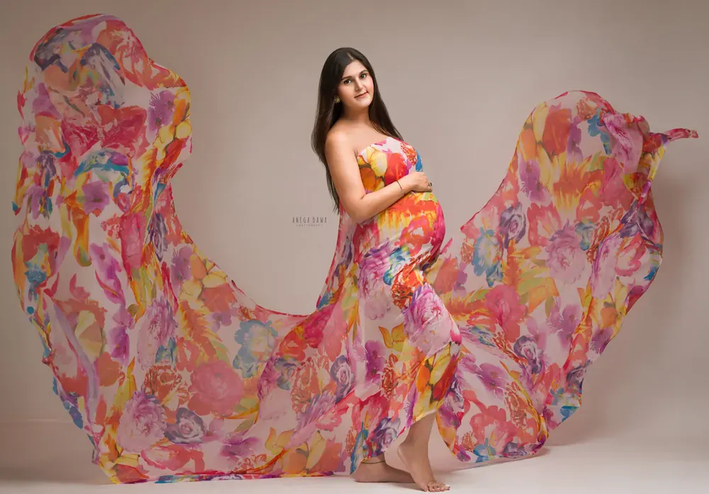 Expecting mother in a strapless bright watercolour floral gown with a huge sheer floral train spread out on both sides, barefoot, hand on