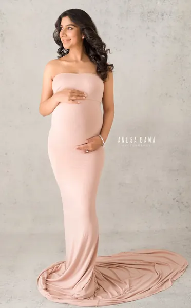 Expecting mother in a dusty pink strapless fitted gown with a spread train, looking to the side, hand on her bump, concrete textured light
