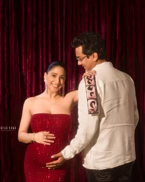 Maternity photoshoot in Delhi: smiling expecting mother in a red sequin gown while her husband holds ultrasound scan strips on his