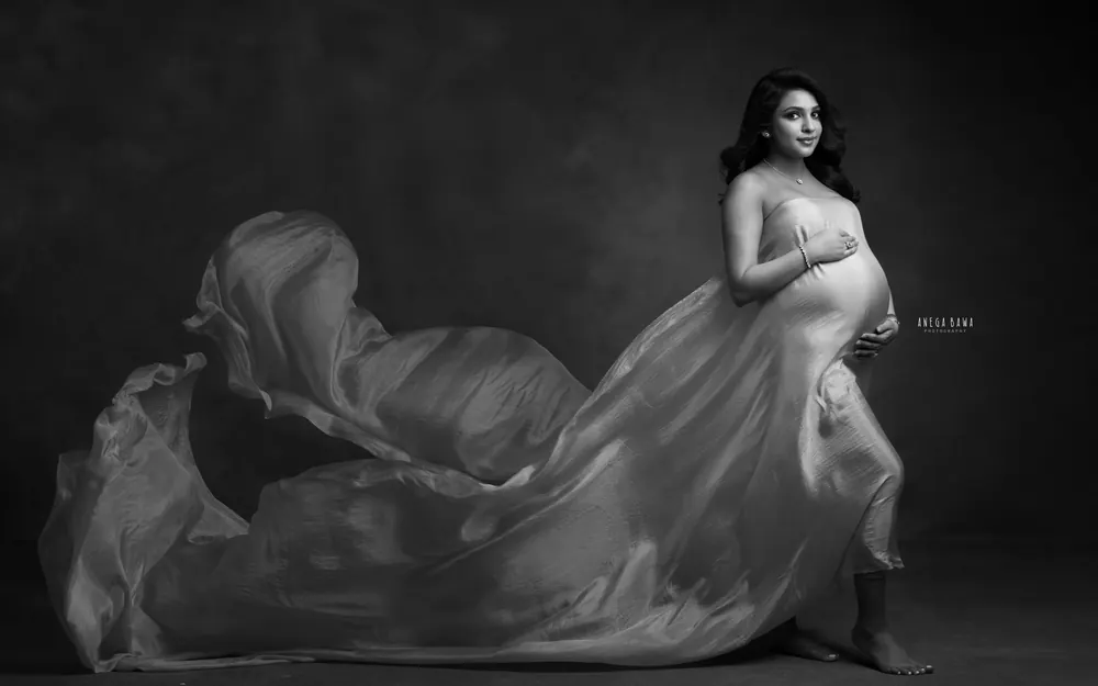 Maternity photoshoot in Delhi: black and white portrait of expecting mother in a strapless silk drape with the fabric flowing out behind
