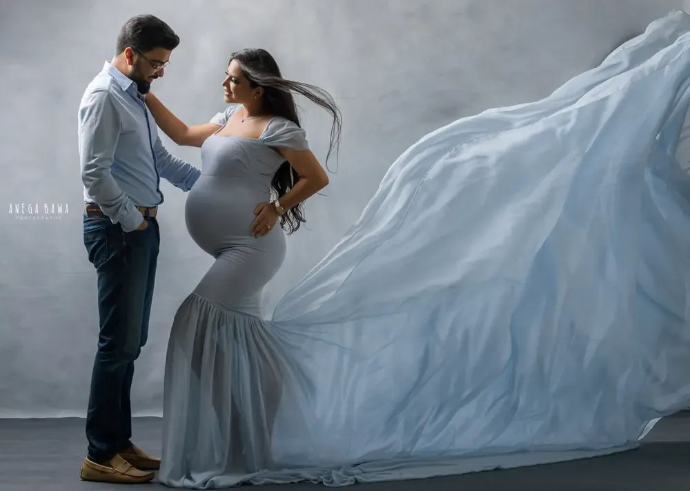 Couple portrait: husband in a light blue shirt and jeans with his hand in his pocket looking at his wife, wife in a dusty blue off-shoulder