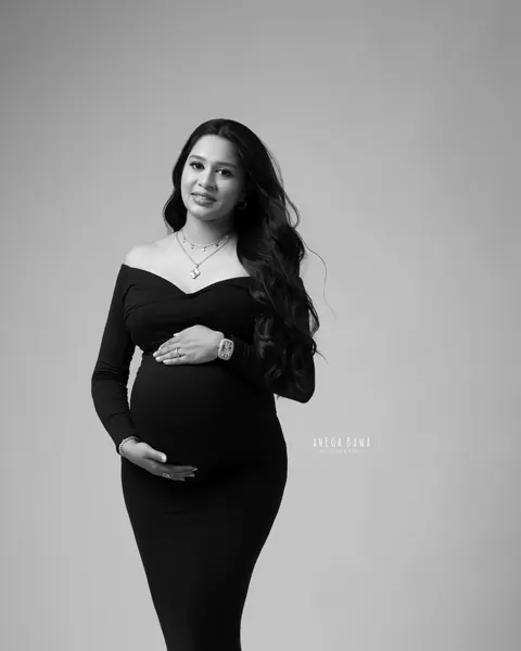Maternity photoshoot in Gurgaon: black and white full-length portrait of expecting mother in a fitted off-shoulder black gown with a long