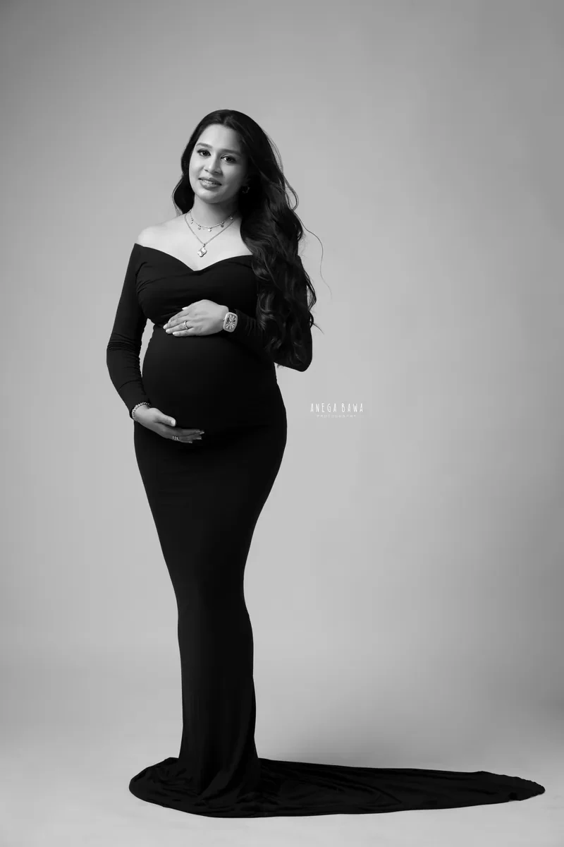 Maternity photoshoot in Gurgaon: black and white full-length portrait of expecting mother in a fitted off-shoulder black gown with a long