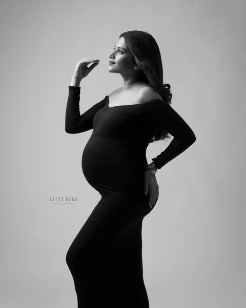 Maternity photoshoot in Gurgaon: black and white profile of expecting mother in a fitted off-shoulder black gown with a train, one hand