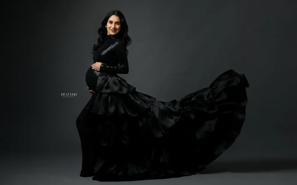 Maternity photoshoot in Gurgaon: expecting mother in a black sequin gown with a tiered black satin ruffle train swept out behind her