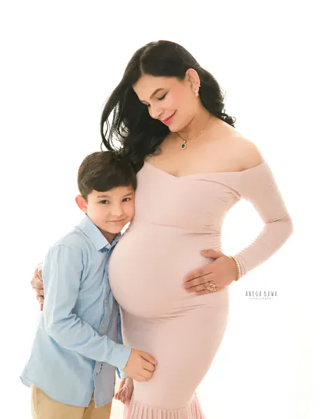 Maternity photoshoot in Gurgaon: expecting mother in a blush pink off-shoulder mermaid gown with her young son leaning against her bump