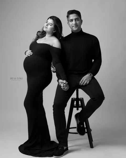 Maternity photoshoot in Gurgaon: black and white full-length portrait of a couple holding hands, wife in a fitted black gown with a train