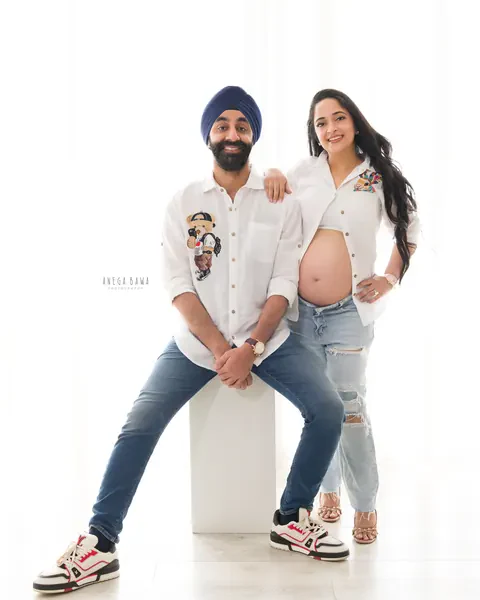 Maternity photoshoot in Gurgaon: couple in matching white embroidered shirts and denim, husband in a navy turban seated on a white block