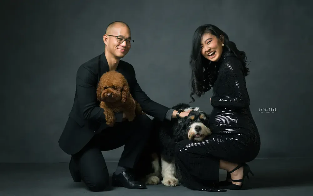 Maternity photoshoot in Gurgaon: laughing expecting mother in a black sequin dress kneeling beside her husband, who holds one small dog