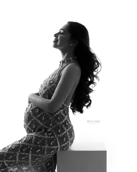 Maternity photoshoot in Gurgaon: black and white silhouette of expecting mother seated on a white block in profile, face lifted, wearing a
