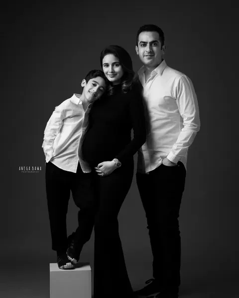 Maternity photoshoot in Gurgaon: black and white family portrait, expecting mother in a black gown with her son leaning on her shoulder and