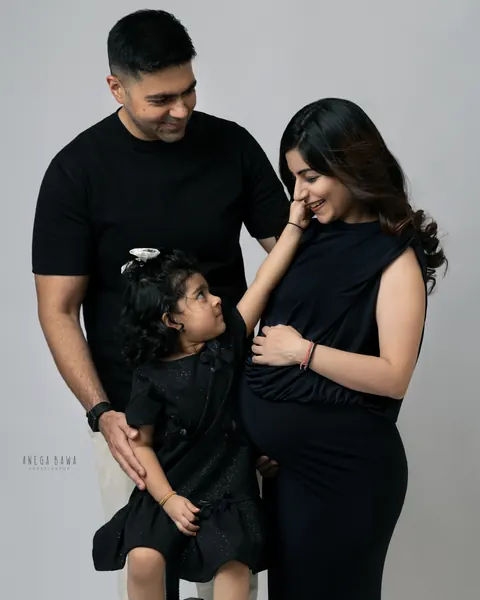 Maternity photoshoot in Gurgaon: family in black outfits, toddler reaching up to touch her mother's face while father looks on, grey