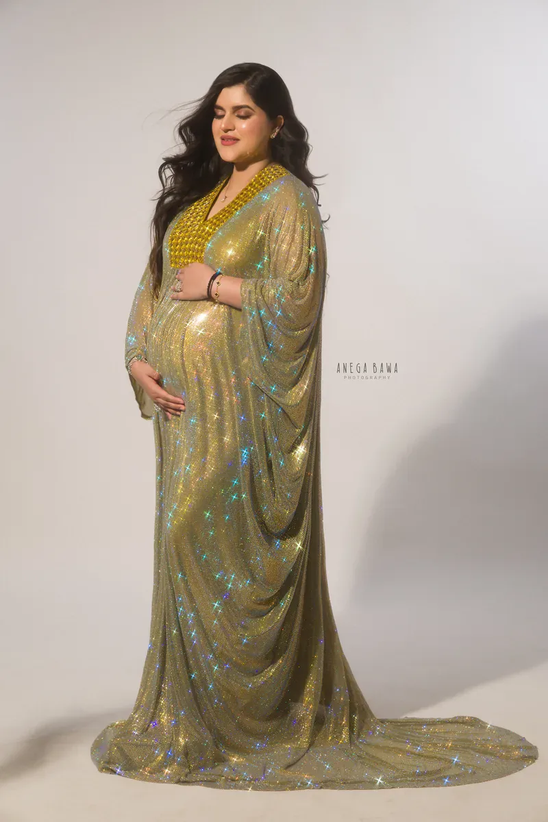 Maternity photoshoot in Gurgaon: full-length portrait of expecting mother with eyes closed in a sparkling gold kaftan gown with draped