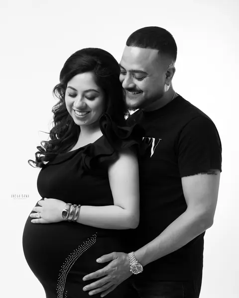 Maternity photoshoot in Gurgaon: black and white portrait of a smiling couple looking down at the bump, husband hugging from behind, wife