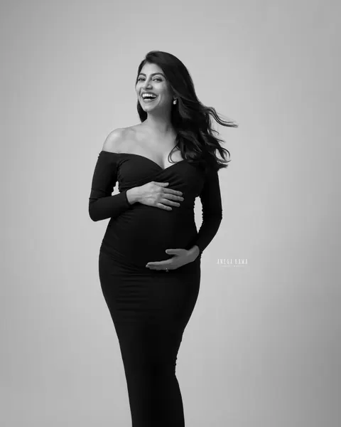 Maternity photoshoot in Gurgaon: black and white full-length portrait of laughing expecting mother in a fitted off-shoulder black gown with
