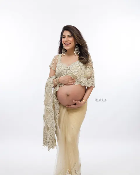 Maternity photoshoot in Gurgaon: laughing expecting mother in a full-length champagne pearl-embroidered net saree with chandelier earrings