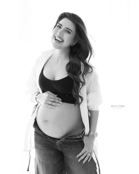 Maternity photoshoot in Gurgaon: black and white portrait of laughing expecting mother in an open white shirt, sports top and low-rise