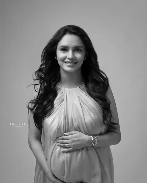 Maternity photoshoot in Gurgaon: black and white portrait of smiling expecting mother in a sheer draped halter dress, hands cradling her