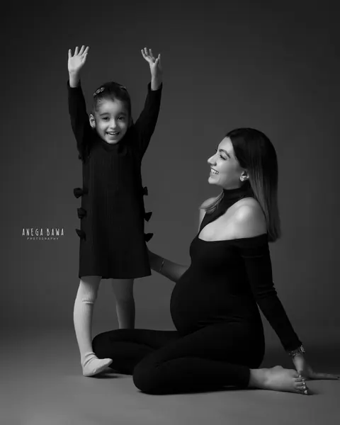 Maternity photoshoot in Gurgaon: black and white portrait of a young daughter with her arms raised, smiling, beside her expecting mother