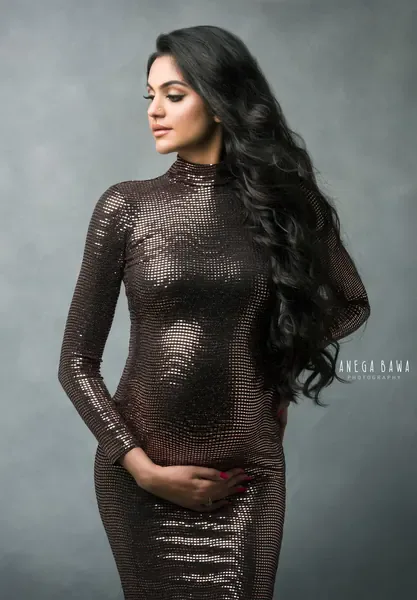 Expecting mother in a fitted bronze sequin high-neck long-sleeve gown, long wavy black hair, looking to the side, hand on her bump