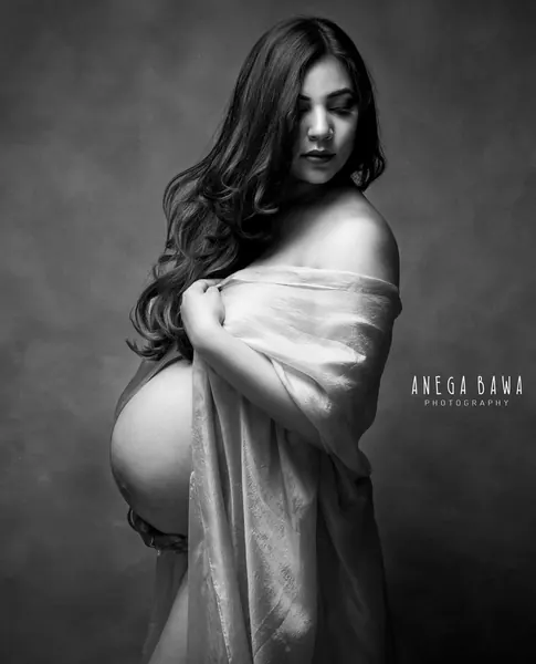 Black and white portrait of expecting mother with long wavy hair falling across her face, wrapped in a loose cloth with bare shoulders