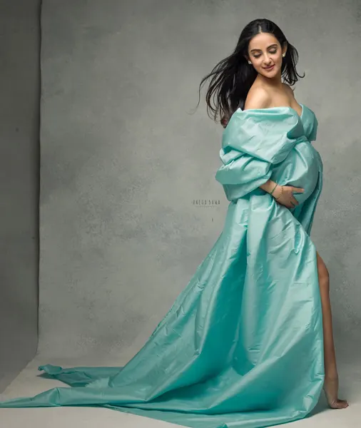 Expecting mother in a soft aqua taffeta robe-style gown slipping off one shoulder with a long train and high slit, hair blowing, textured