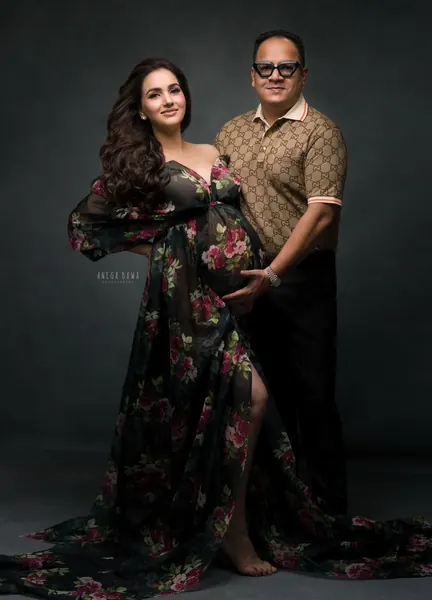 Couple portrait, wife in a sheer dark rose-print gown with a high slit and big sleeves, husband in a monogram polo and black trousers