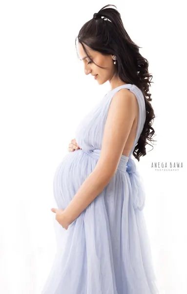 Expecting mother in profile in a pale lilac-blue tulle halter gown with a bow at the back, hair in a high half-updo, looking down, hands