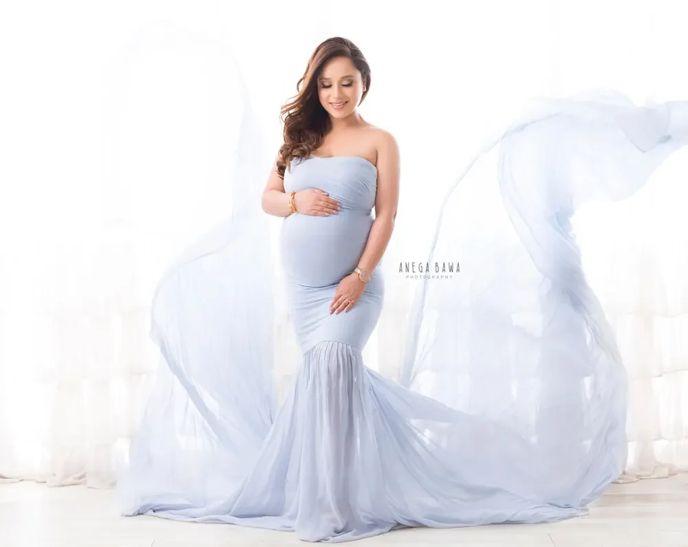 Expecting mother in a pale blue strapless mermaid gown with a sheer blue train flying out around her, hands on her bump, bright white