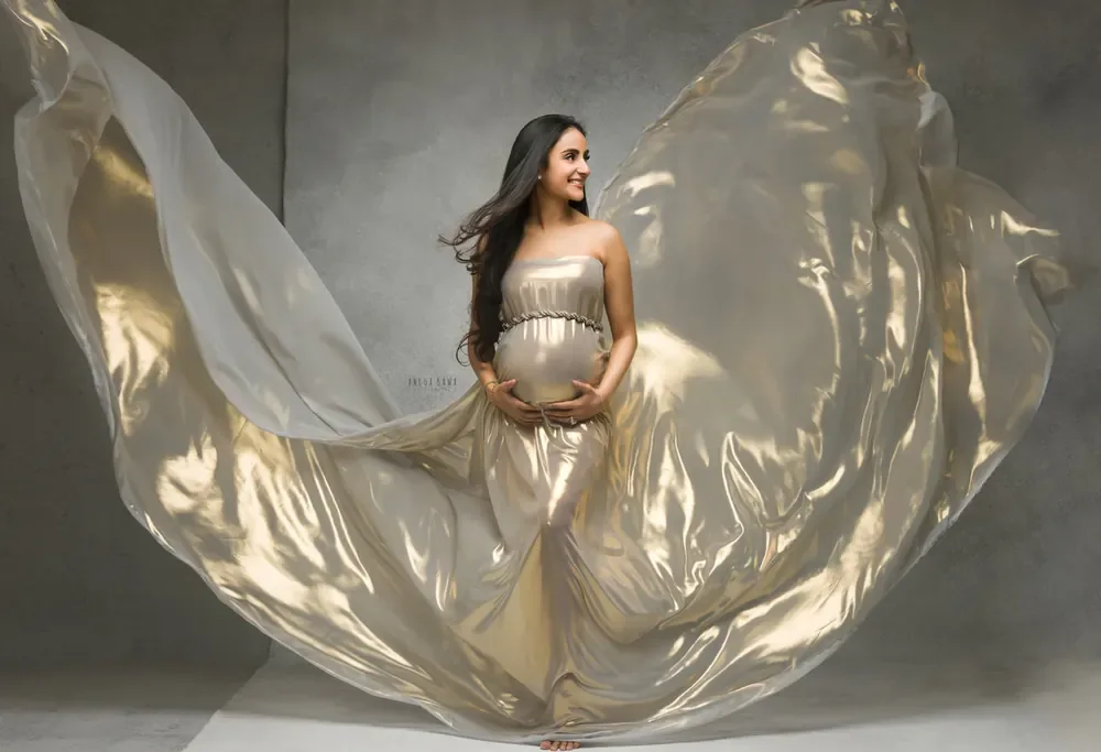 Expecting mother in a champagne-gold strapless gown with a beaded belt and a vast metallic gold sheer train flying out in wings on both