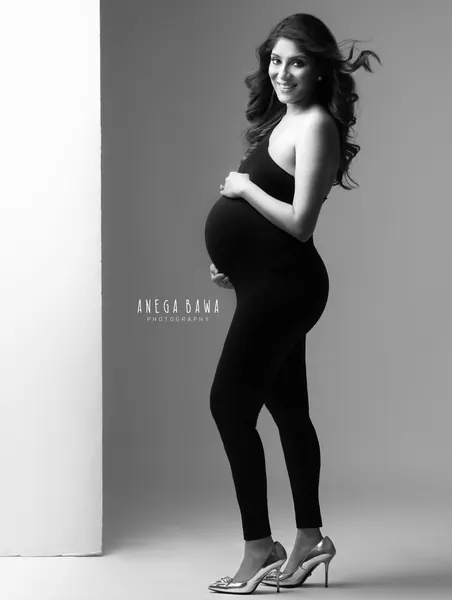 Black and white portrait of smiling expecting mother in profile in a black halter jumpsuit and metallic heels, hand on her bump, hair