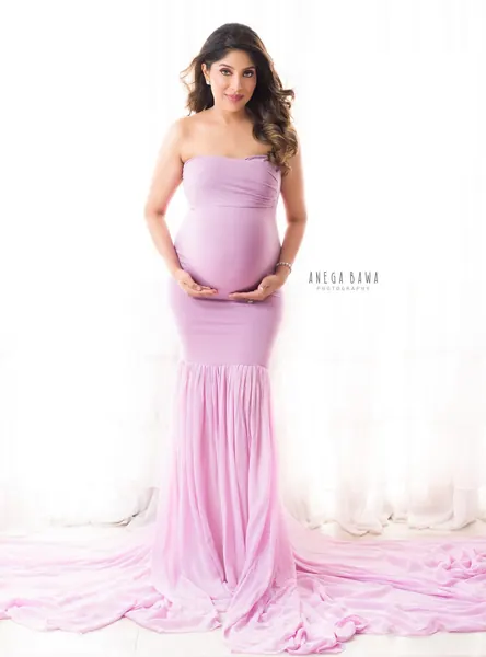 Expecting mother in a lilac strapless fitted mermaid gown with a long chiffon train spread on the floor, hands on her bump, bright white