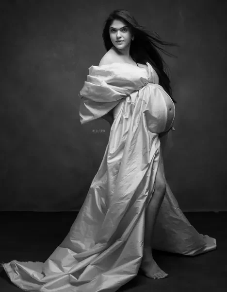 Black and white portrait of expecting mother in a satin gown wrapped off the shoulders with puffed sleeves and a long train, hair blowing
