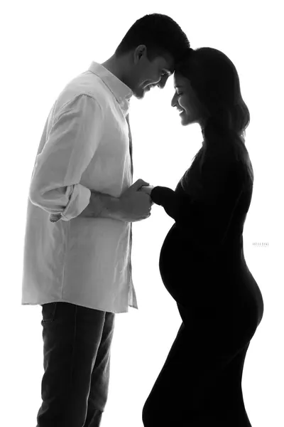 High-key black and white silhouette of a couple touching foreheads and holding hands, husband in a rolled-sleeve shirt and jeans, wife in a