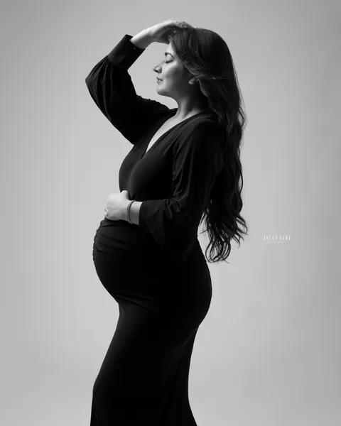 Pregnancy photoshoot in Delhi: black and white profile of expecting mother in a black V-neck gown with one hand on her head and one on her