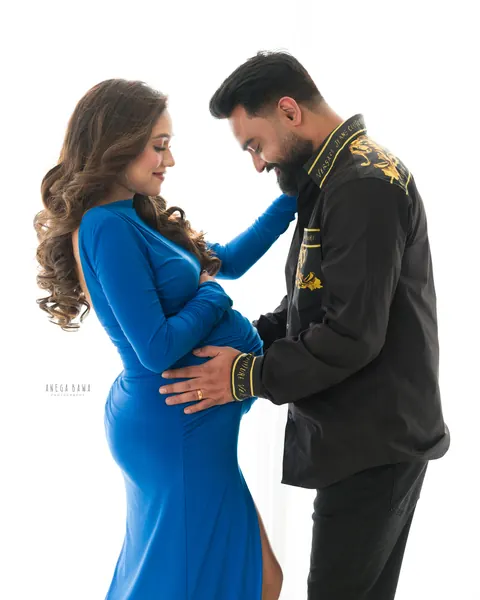 Pregnancy photoshoot in Delhi: expecting mother in a royal blue gown with her husband in a black embroidered shirt, both looking down at