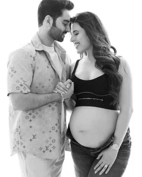Pregnancy photoshoot in Delhi: black and white portrait of a couple touching foreheads and holding hands, wife in a sports top and low-rise