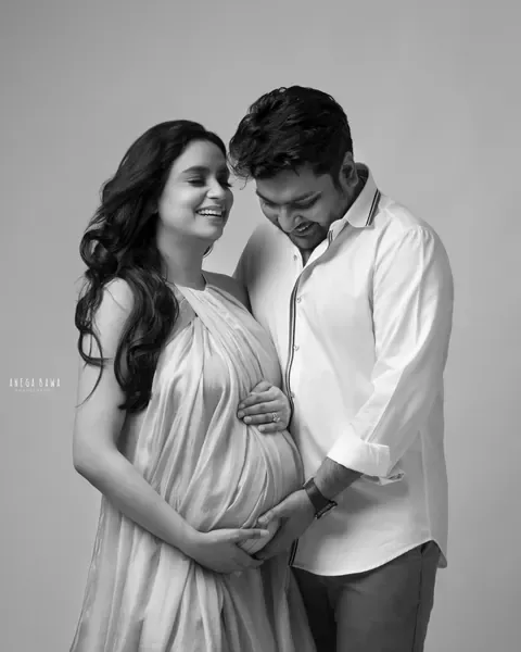 Pregnancy photoshoot in Delhi: black and white portrait of a laughing couple, wife in a sheer draped halter dress and husband in a white
