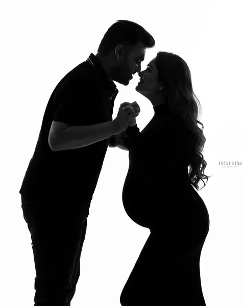 Pregnancy photoshoot in Delhi: black and white silhouette of a couple touching noses and holding hands, her bump in profile, white